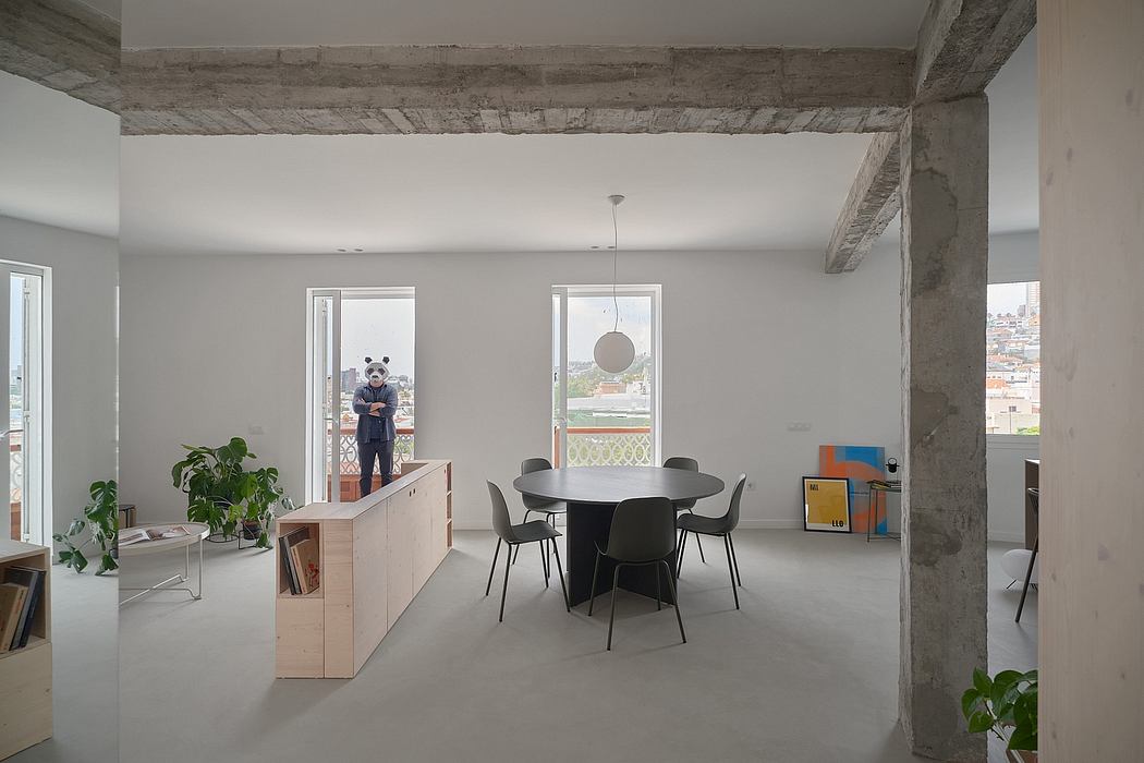 Loft-style apartment with exposed concrete beams, minimalist furnishings, and large windows.
