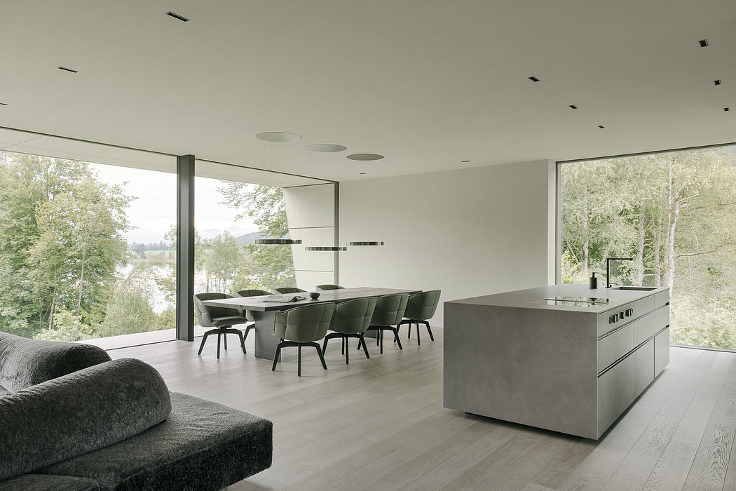 Modern, open-plan kitchen and dining area with large windows offering scenic forest views.