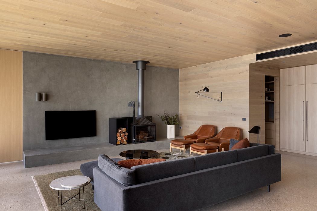 Modern, minimalist living room with wood-paneled ceiling, concrete fireplace, and sleek leather furniture.