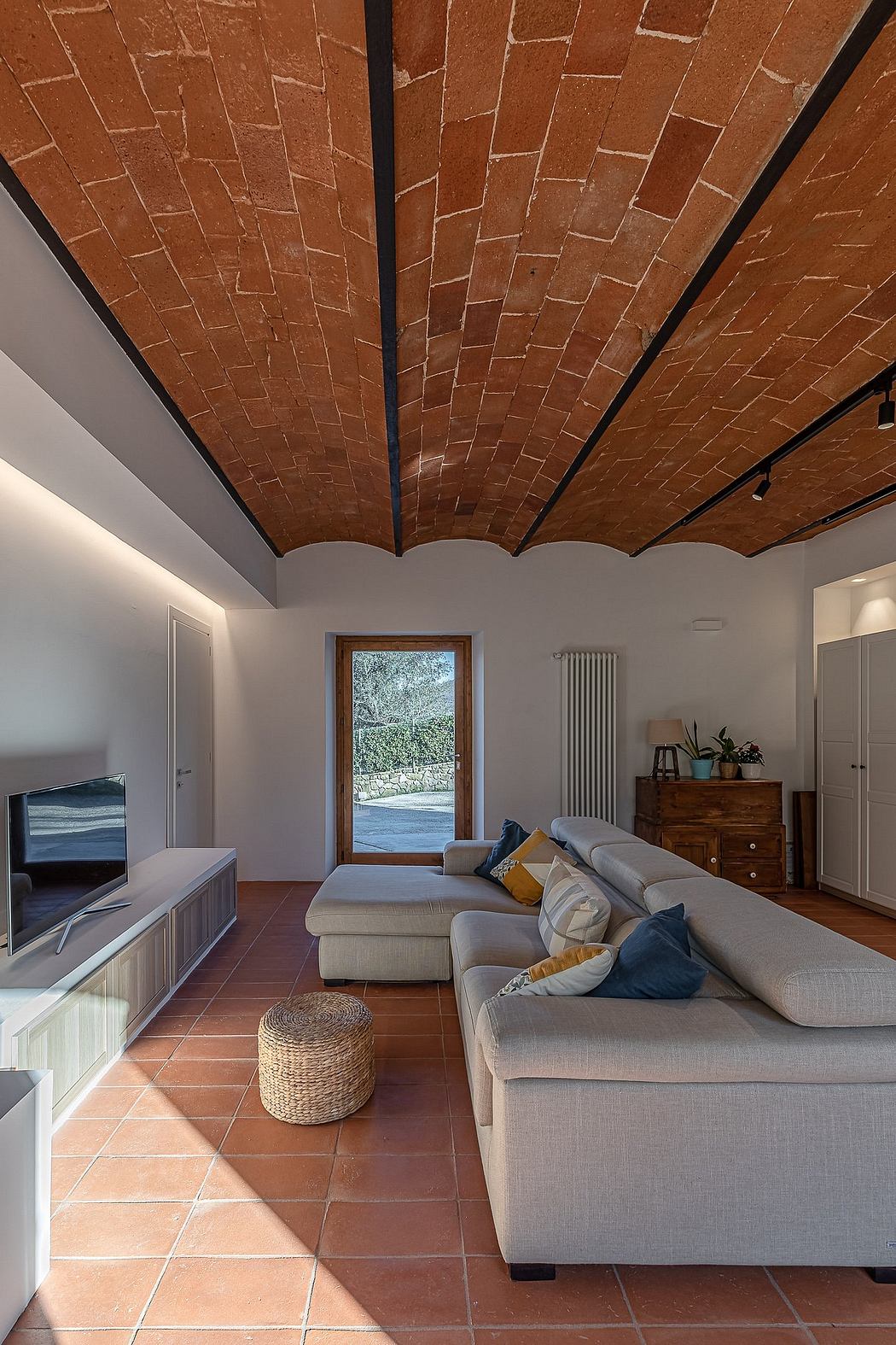 Striking red brick ceiling and terracotta tile flooring in cozy living room with natural lighting.