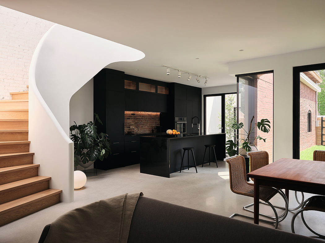 A modern, minimalist kitchen with black cabinetry, wood accents, and a curved staircase.