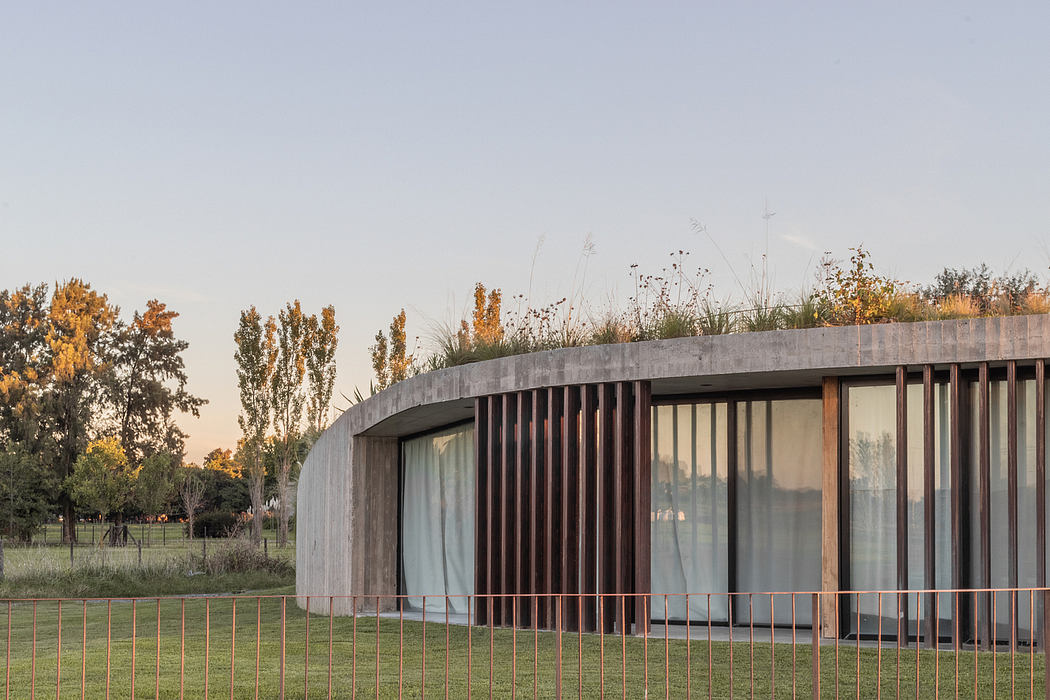 A modern, curved concrete structure with glass walls and wooden slats, situated in a lush, autumnal landscape.