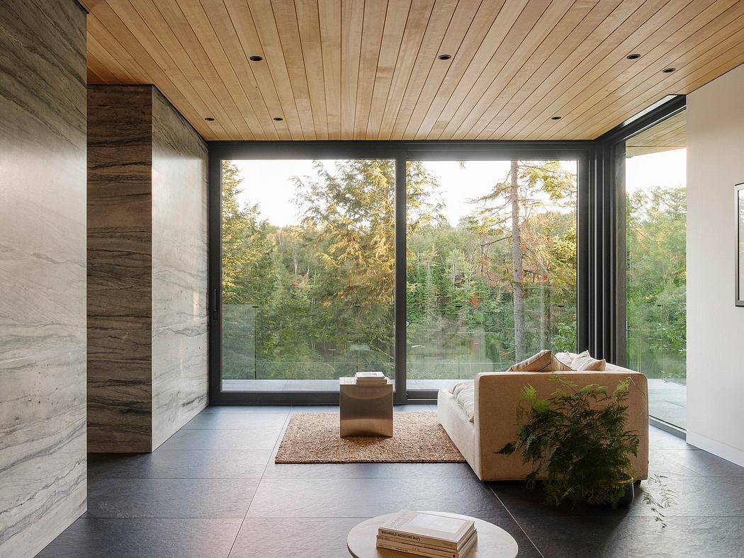 Large windows overlooking a wooded landscape, with a wooden ceiling and minimalist furnishings.