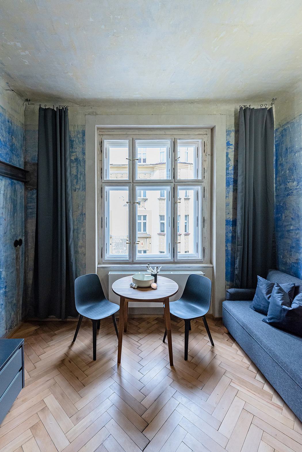 Bright, modern room with large window, herringbone wood floor, and minimalist furniture.