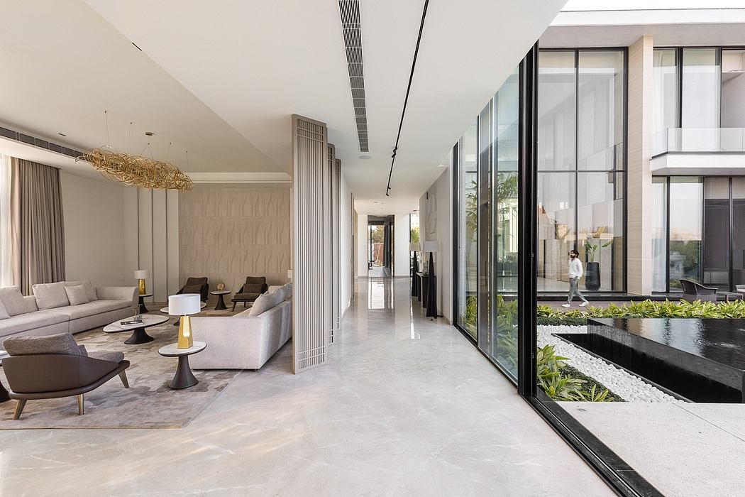 Spacious, modern interior with sleek furniture, lighting fixtures, and floor-to-ceiling windows overlooking a water feature and greenery.