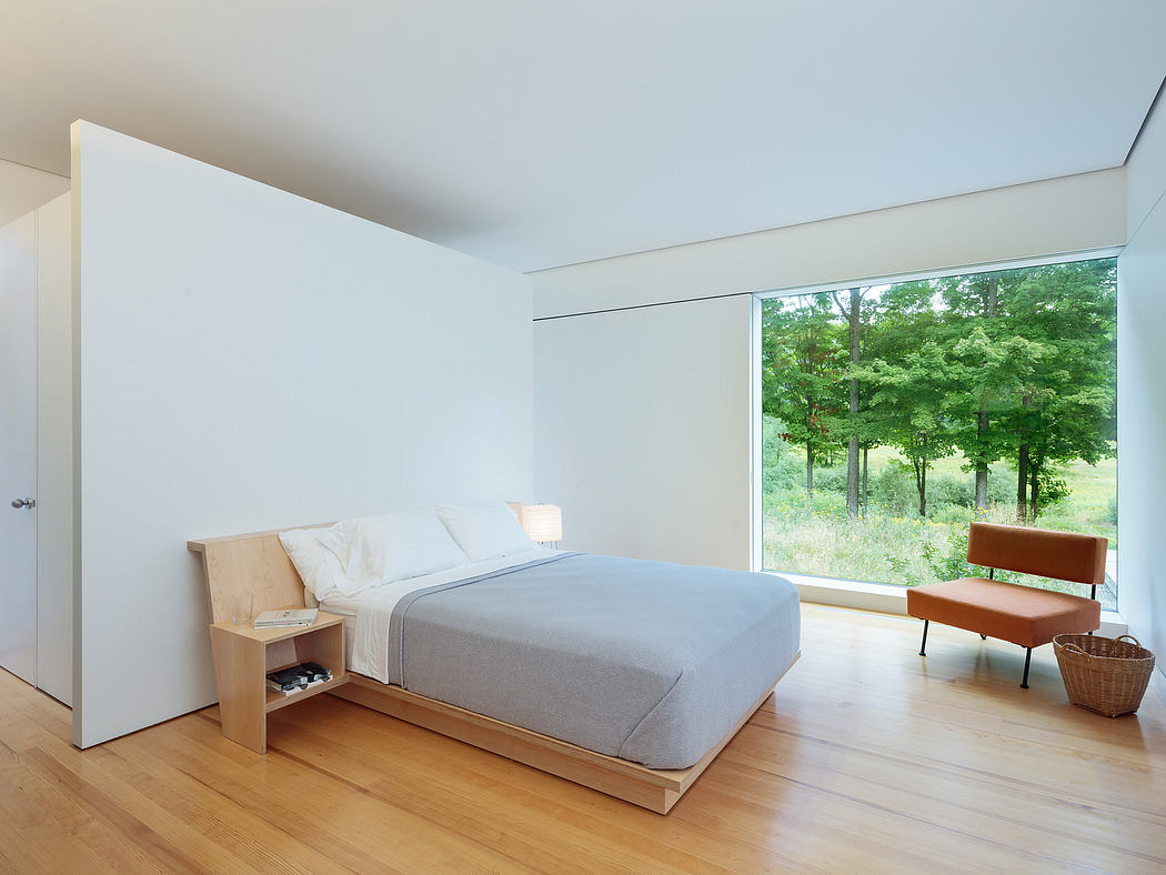 Modern bedroom with large window overlooking lush greenery, minimalist furnishings.