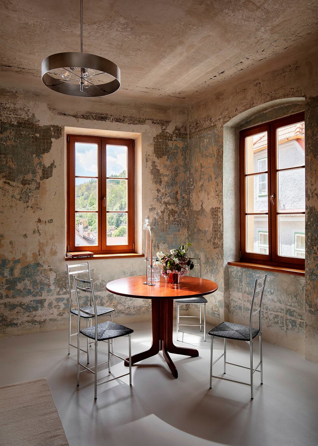 Rustic dining room with peeling plaster walls, circular wooden table, and metal chairs.
