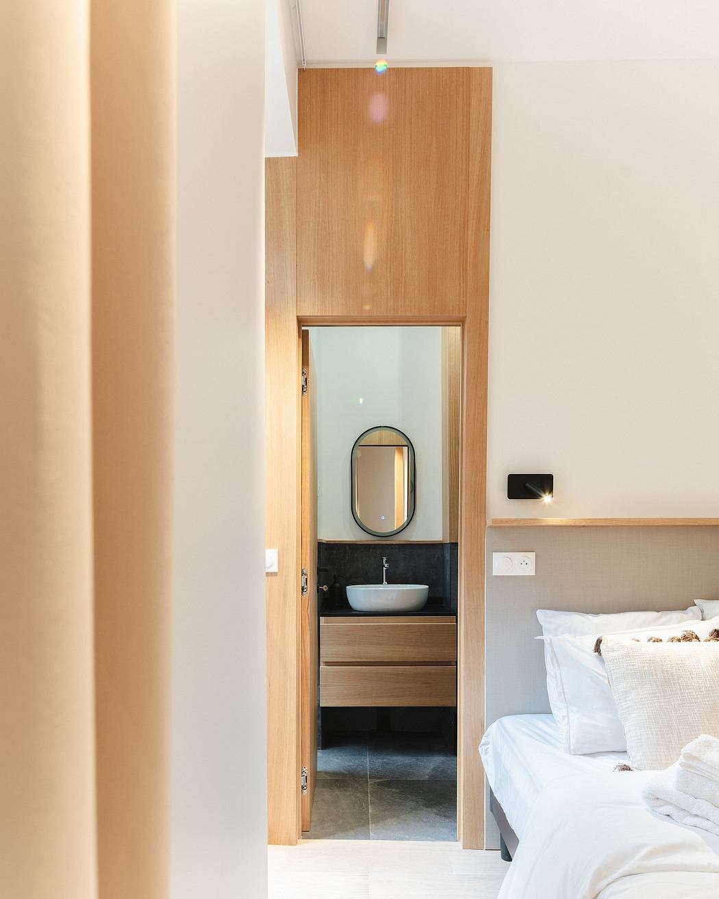 Minimalist bedroom with wooden ensuited bathroom, recessed lighting, and neutral decor.