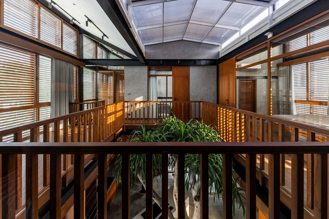 Spacious atrium with wooden railings, glass ceiling, and lush indoor plants.