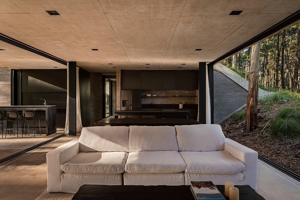 Expansive modern interior with concrete ceiling, wood accents, and large windows overlooking forest.