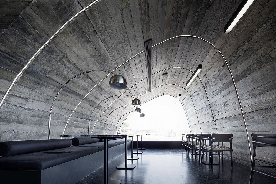 Dramatic concrete structure with curving ceiling, suspended lighting, and minimalist furnishings.