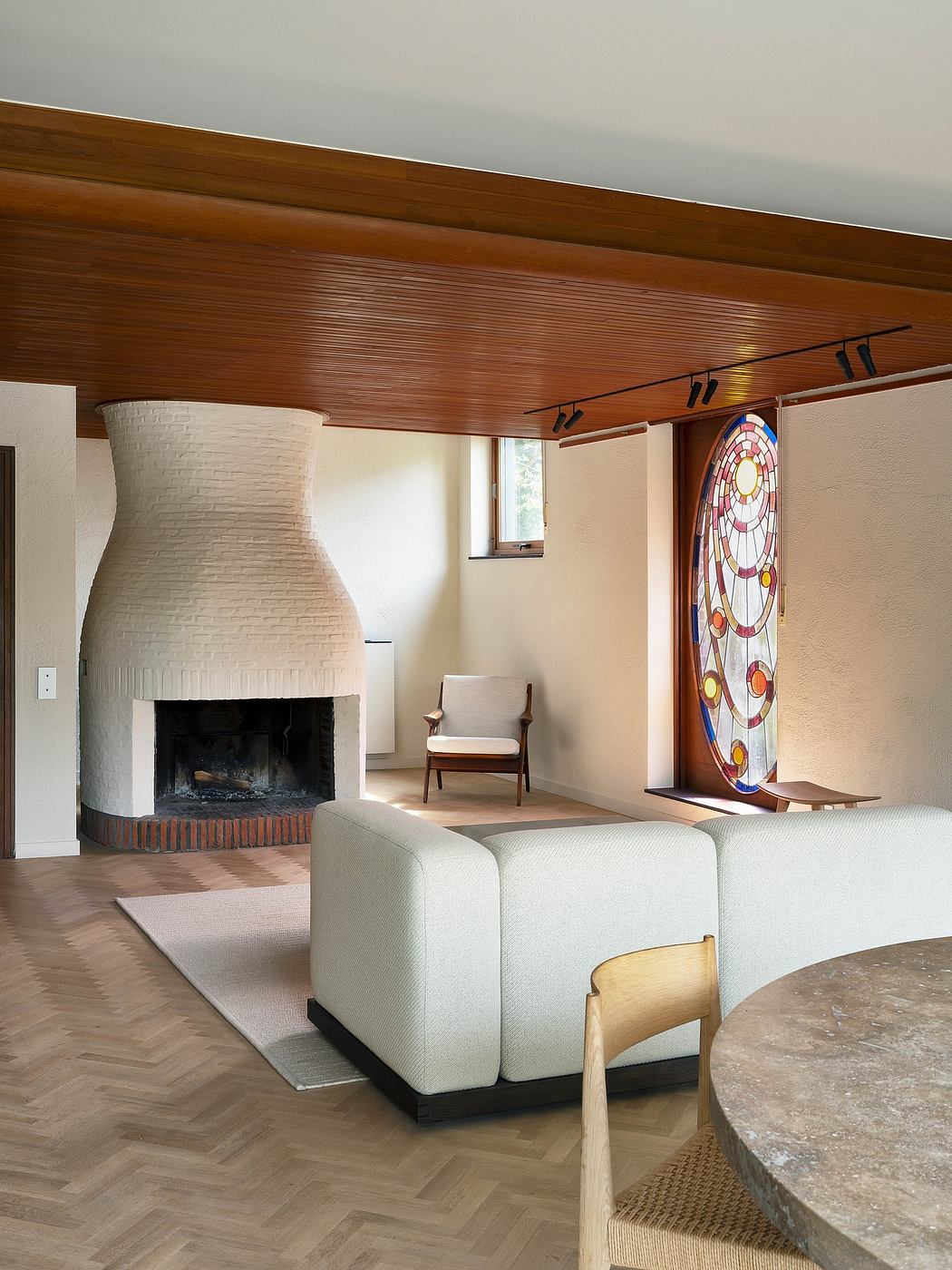 Warm wooden ceiling, white brick fireplace, stained glass window, and modern furniture.