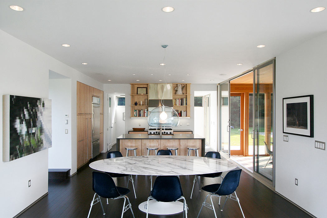 Modern open-concept kitchen with marble dining table, wooden cabinetry, and sleek pendant lighting.