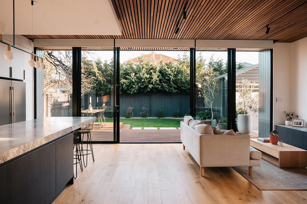 Modern open-concept living space with wooden ceiling, marble countertops, and lush outdoor view.