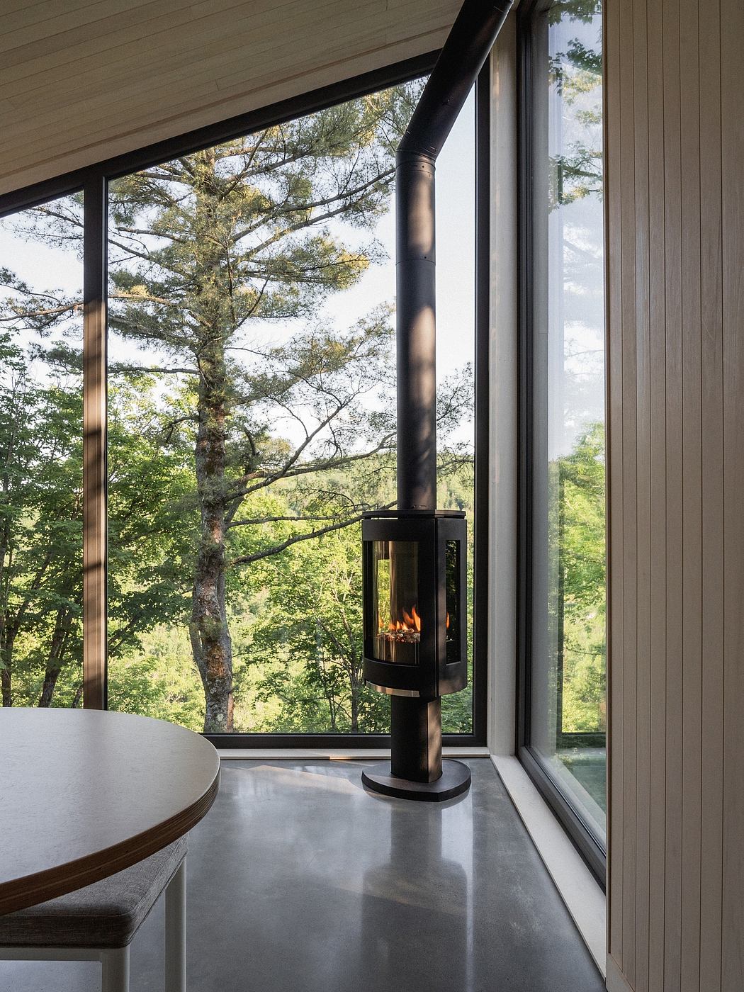 A modern interior design with a wood-burning stove, large windows, and a view of the surrounding nature.