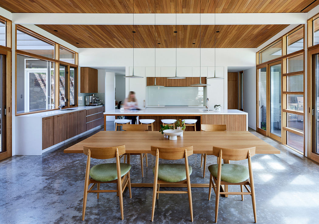 An open-plan kitchen and dining area with wooden accents, large windows, and a modern aesthetic.