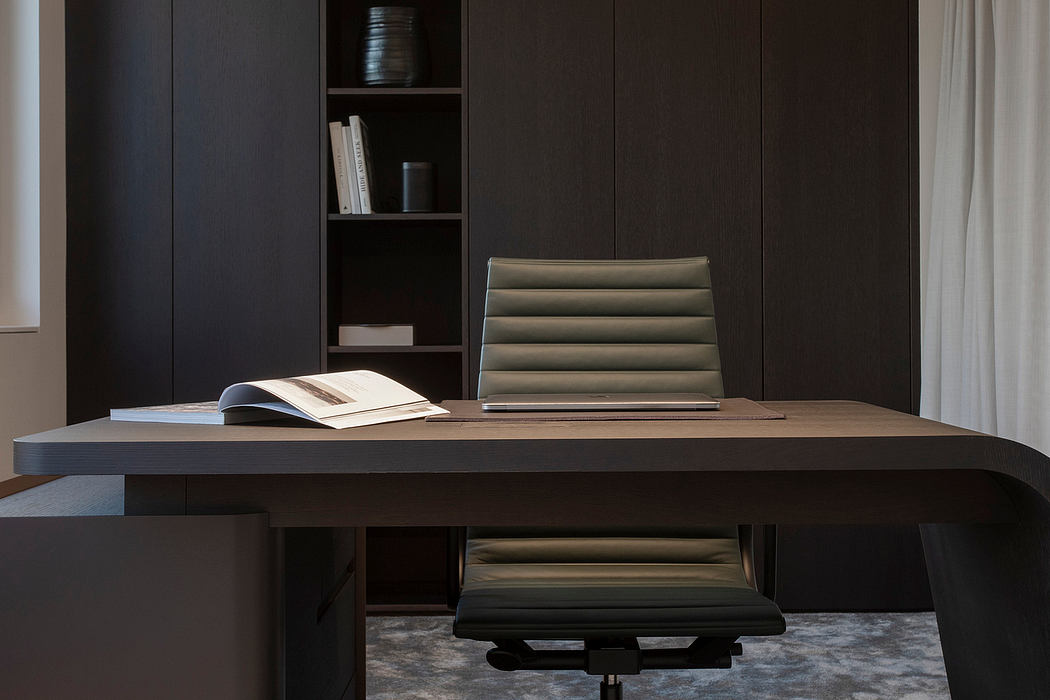 Dark, minimal workspace with wooden desk, upholstered chair, and built-in shelving.