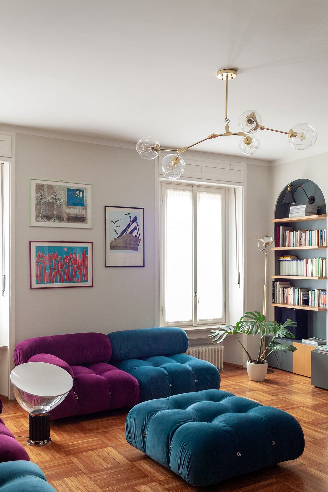 Cozy and colorful living room with tufted velvet couches, modern lighting fixture, and eclectic wall art.