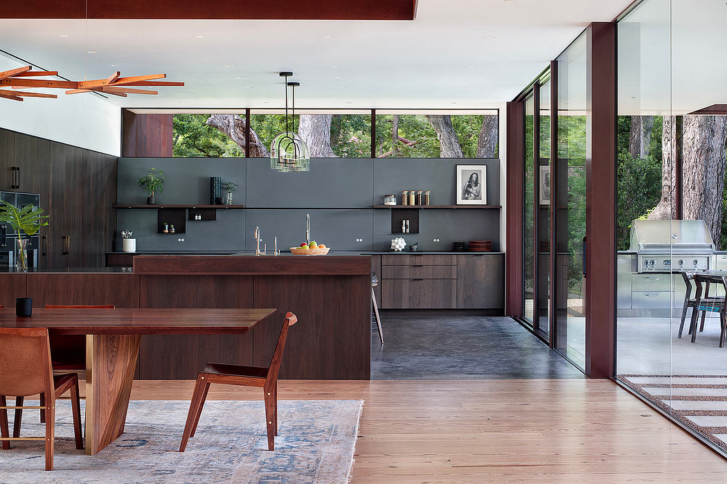 Modern open-concept kitchen with large windows, dark cabinetry, and wooden furniture.