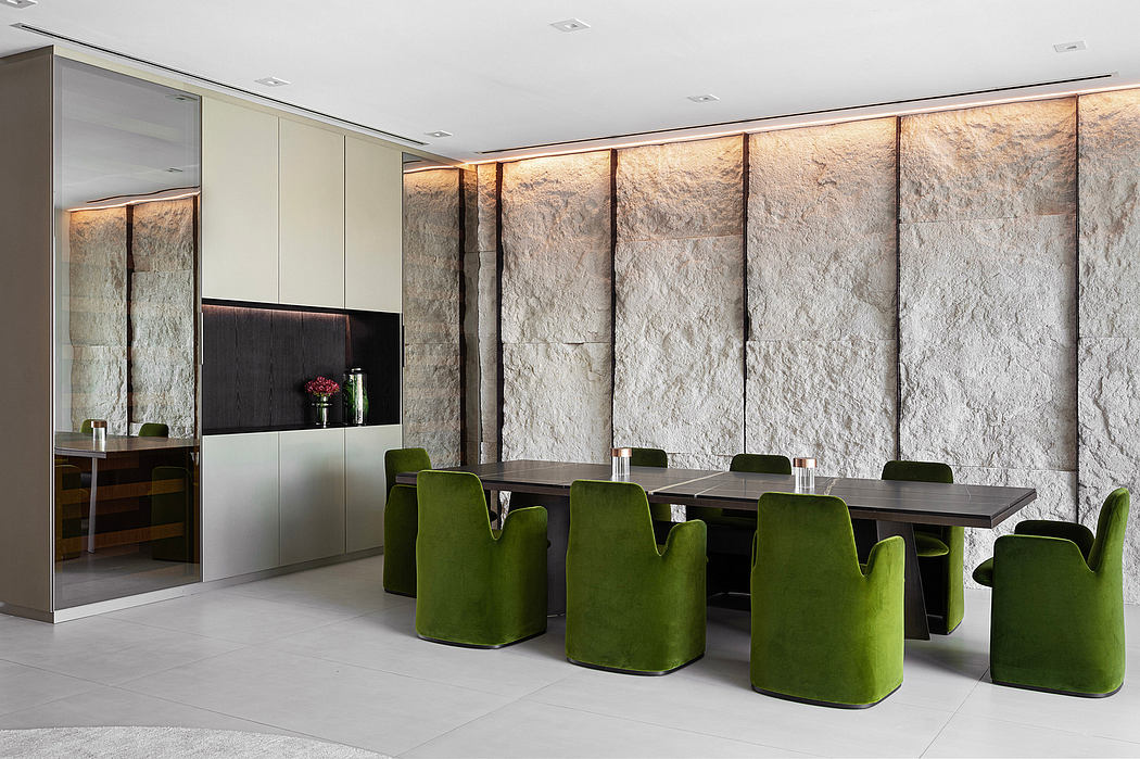 Modern dining space with natural stone walls, sleek wooden table, and plush green chairs.