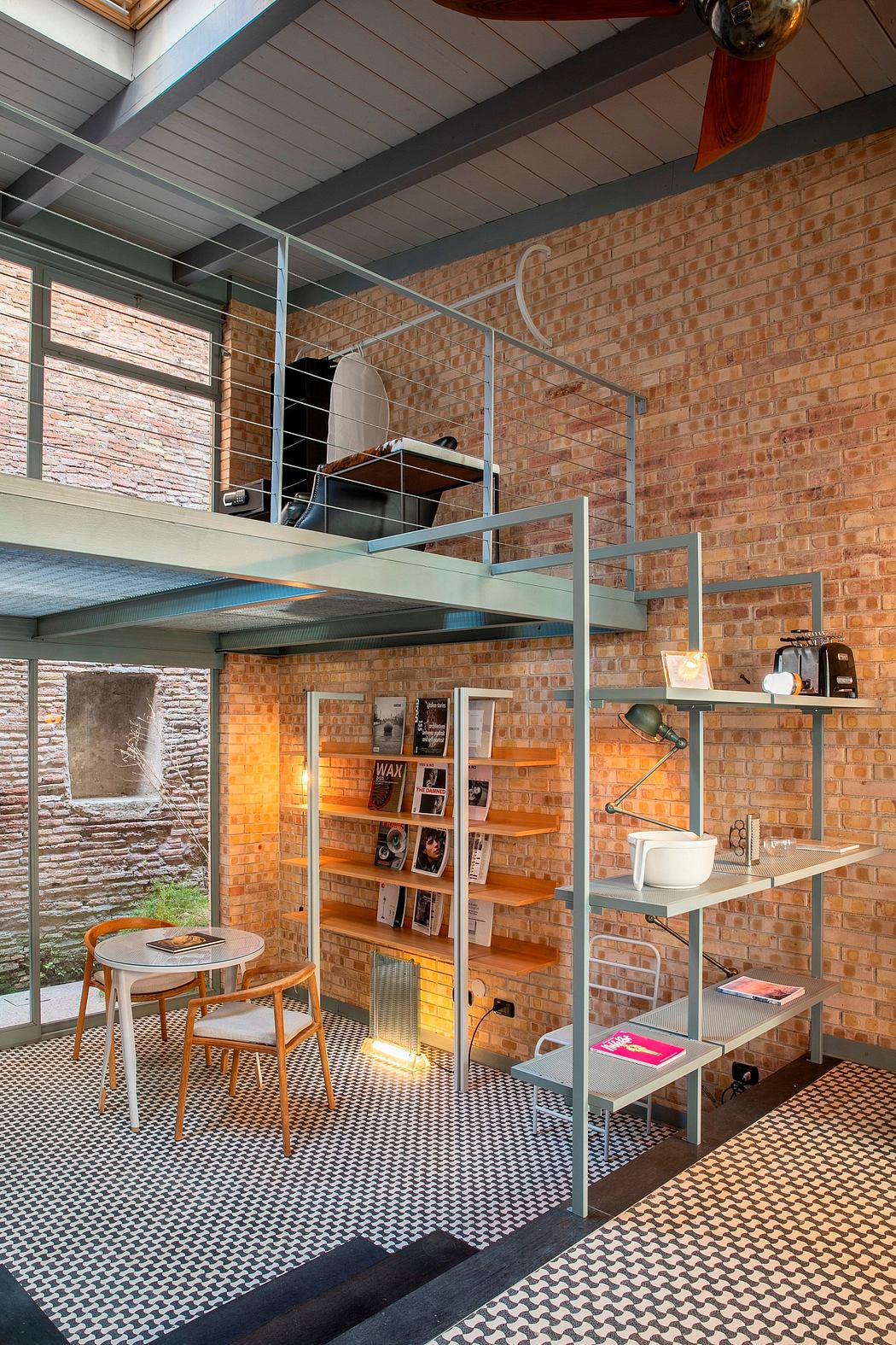 A contemporary loft-style interior with exposed brick walls, open shelving, and a mezzanine level.