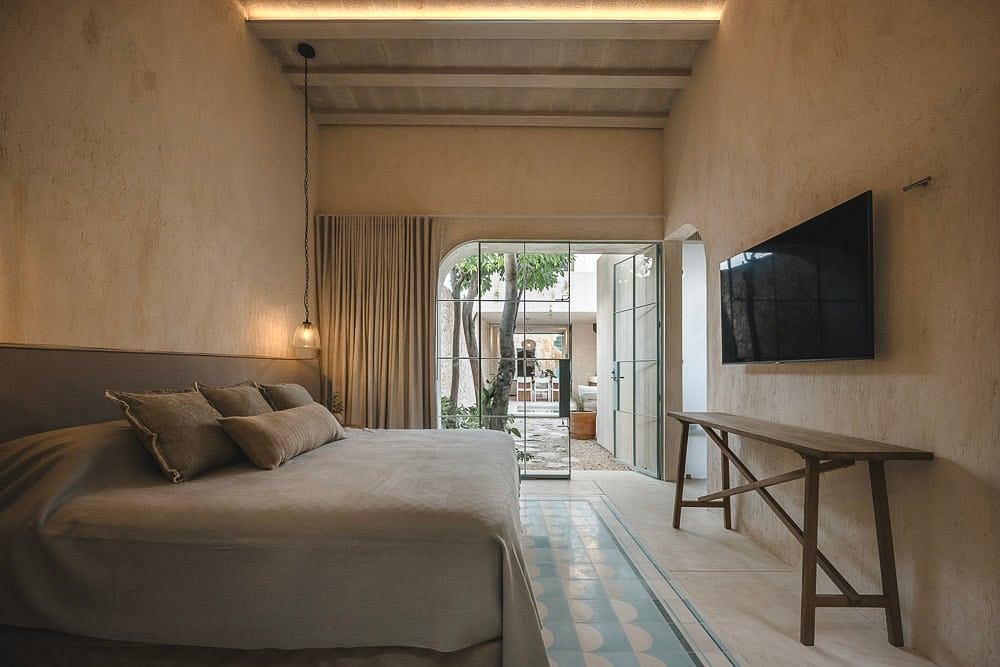 Cozy, rustic bedroom with wood beams, floor-to-ceiling curtains, and a patterned tile floor.