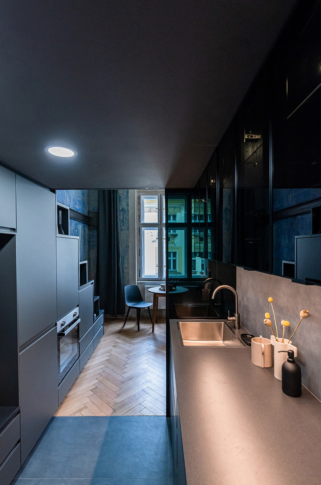 A modern, dark-toned kitchen with built-in appliances, a sink, and a small dining area.