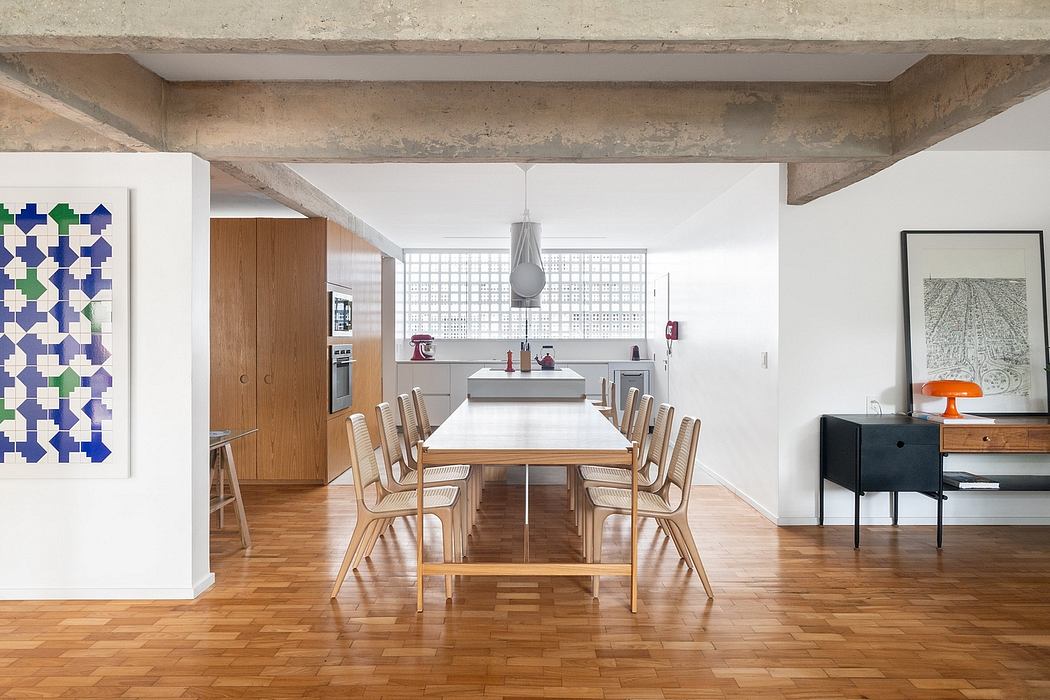Open-concept living space with exposed concrete beams, wooden dining table, and built-in kitchen.