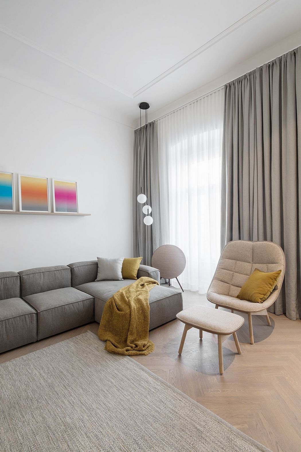 A bright, minimalist living room with gray upholstered sofa, wooden accent chair, and colorful framed art.