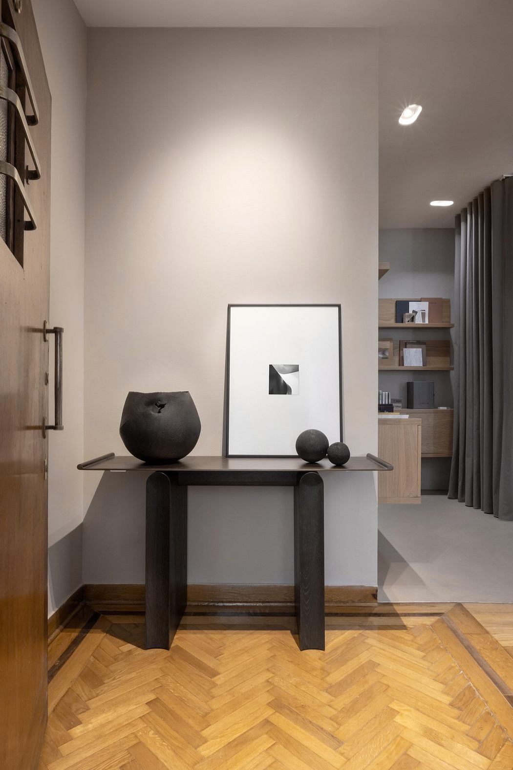 The image depicts a minimalist modern interior design, featuring a simple black console table with abstract sculptures and framed artwork.
