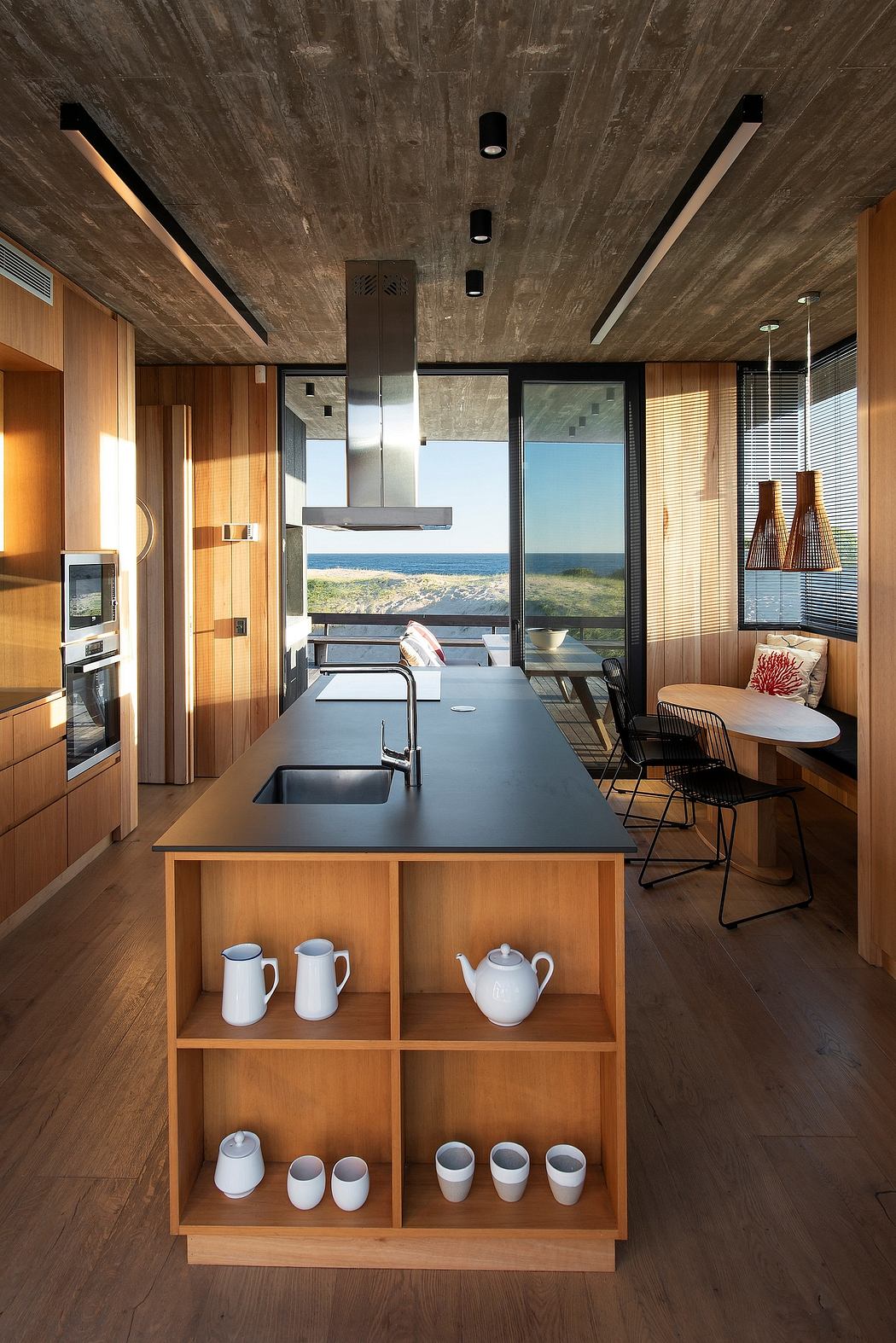 A modern kitchen with minimalist design, dark countertops, and panoramic ocean views.