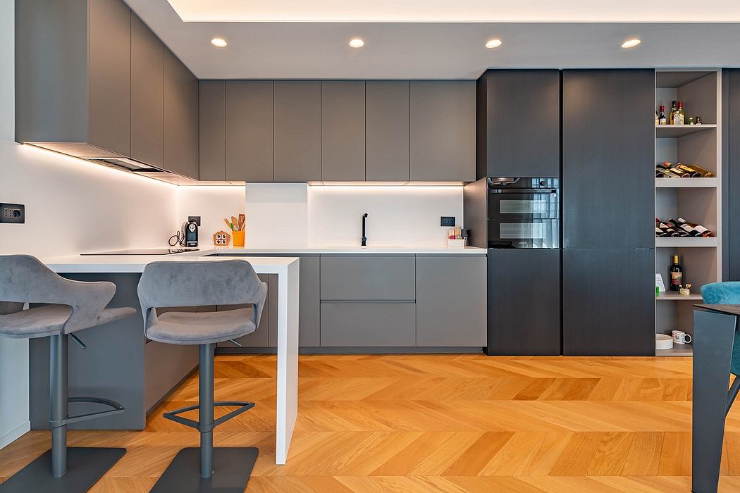Modern kitchen with sleek gray cabinetry, wooden herringbone floors, and built-in appliances.