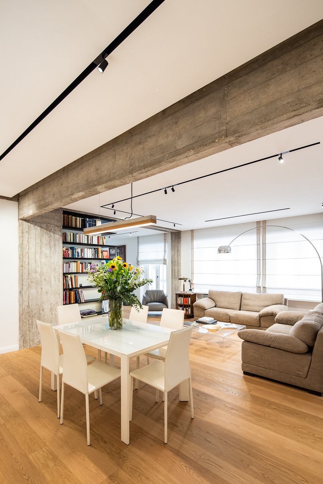 A modern open-plan living room with exposed concrete beams, built-in shelving, and warm wood floors.
