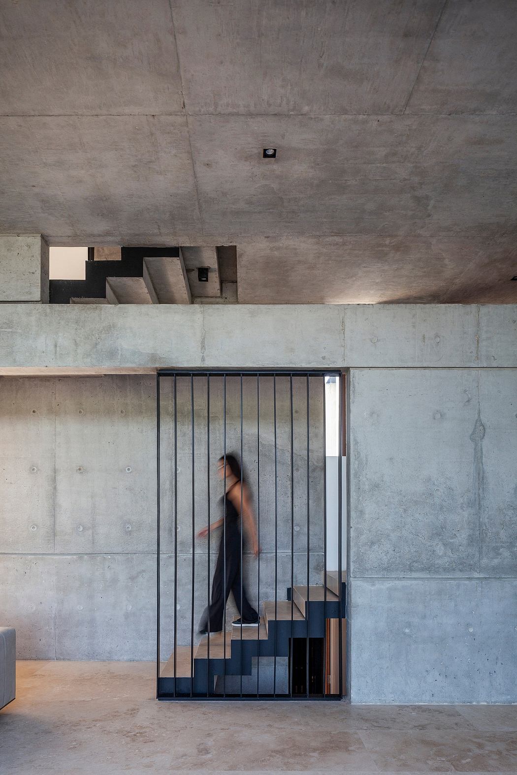 Minimalist concrete interior with angular metal staircase and recessed shelves.