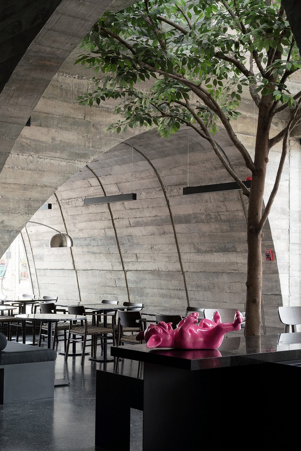 A modern concrete structure with lush greenery, designer furniture, and bold pink sculptures.