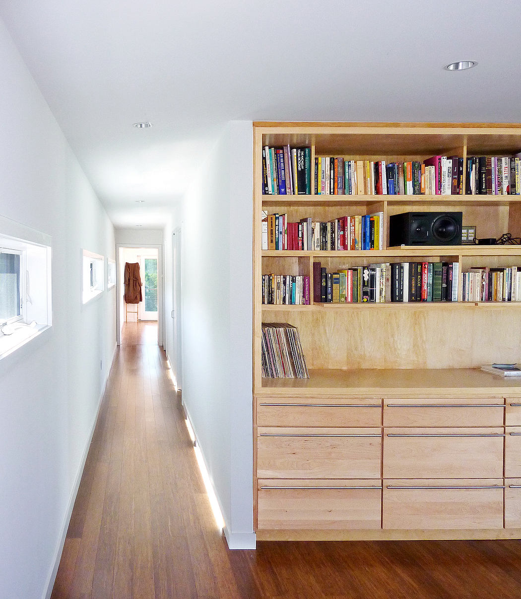 A hallway with hardwood floors leading to a wooden bookshelf filled with books and drawers.