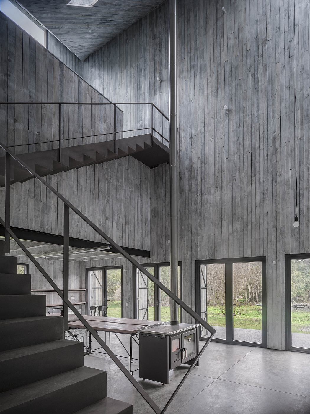 Minimalist architectural design featuring weathered wooden walls, angular stairs, and large windows.