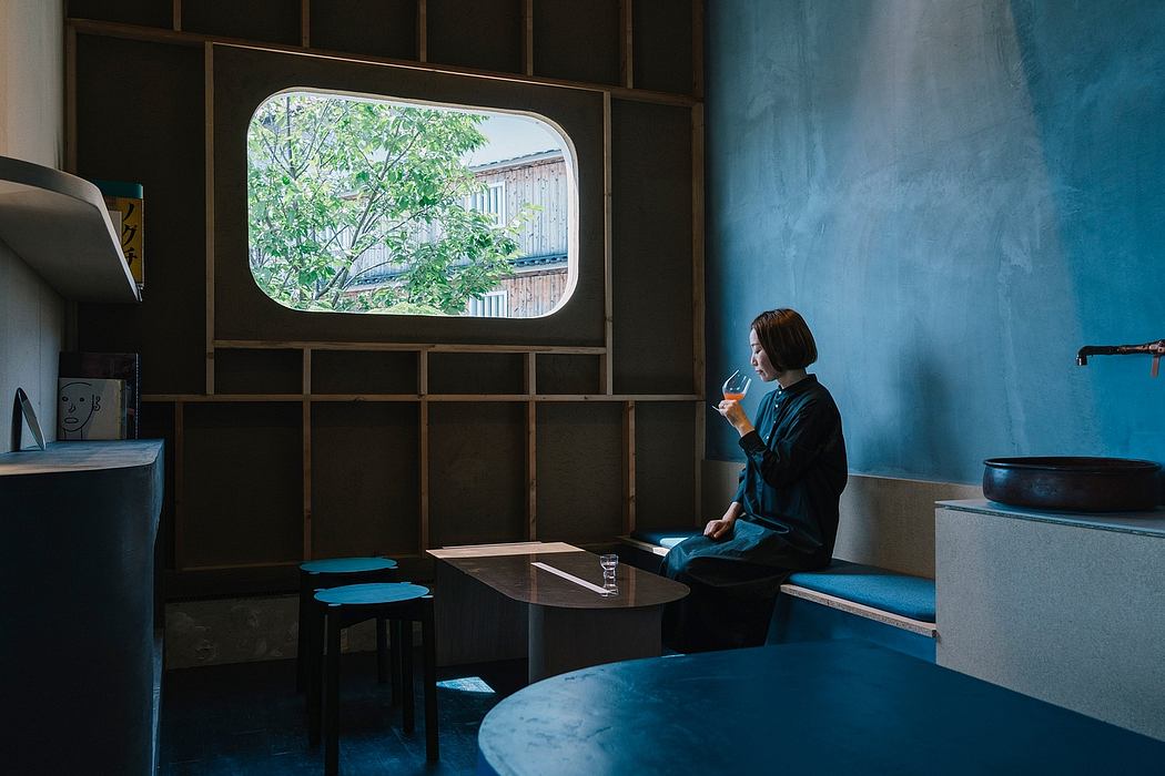 Modern minimalist interior with wooden furniture, blue walls, and window framing a tree-lined view.