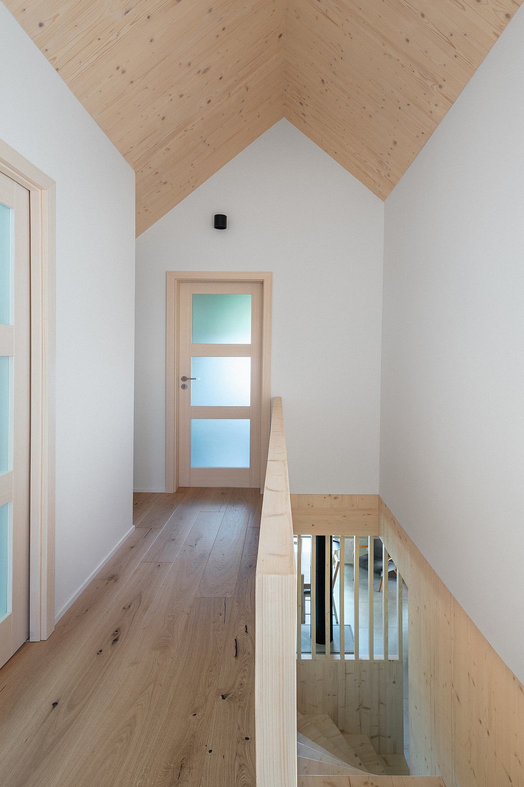 Bright, airy hallway with wooden ceiling and door, wooden floor, and white walls.