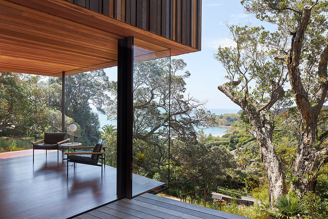 A modern glass-enclosed living space with a panoramic view of a lush, forested landscape.