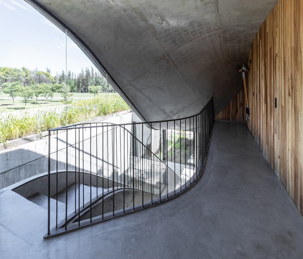 Curved concrete ceiling, wooden walls, and a winding metal balustrade lead to an outdoor view.