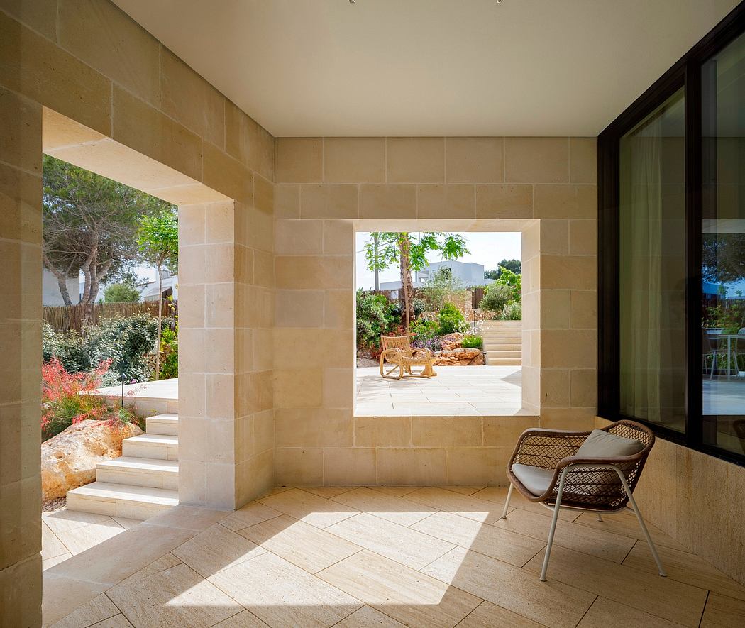 Large stone archway frames a lush, landscaped outdoor patio with a woven rattan chair.
