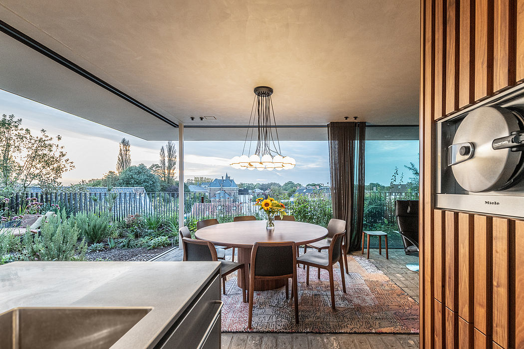 A modern dining area with a round table, chandelier, and glass doors overlooking a lush outdoor garden.