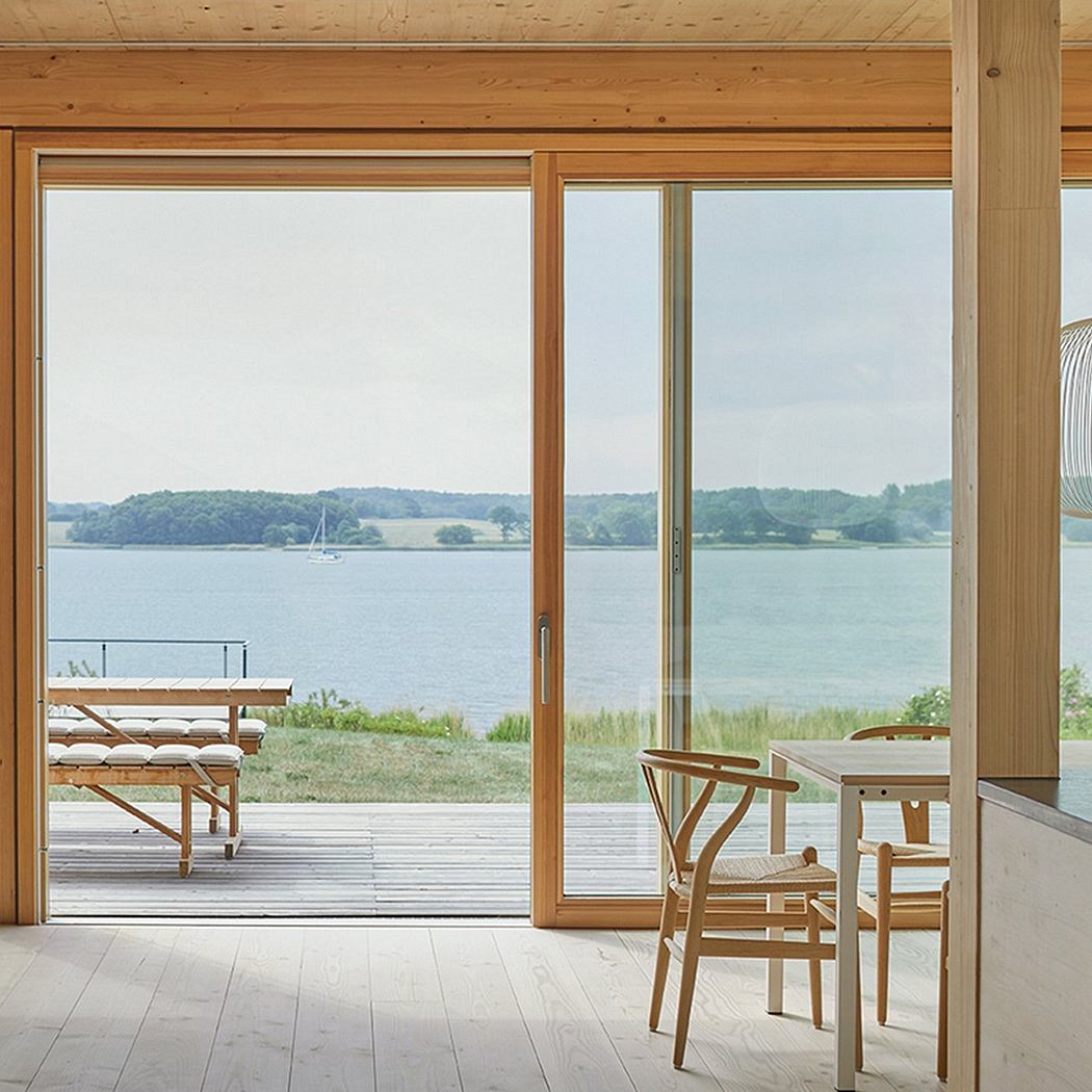 Wooden interior with panoramic lakeside view, simple furniture and natural light.