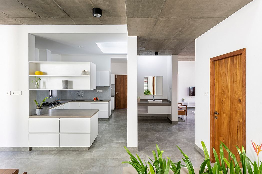 A modern, open-concept kitchen with concrete ceilings, white cabinets, and a wooden door.