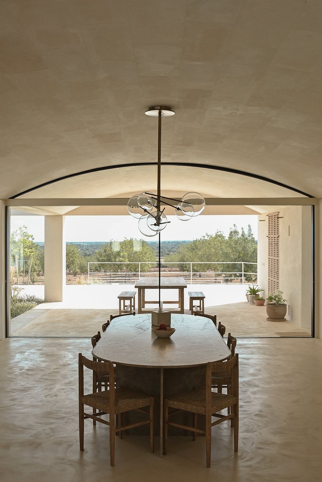 Elegant dining area with arched windows, modern light fixture, and rustic wooden furniture.
