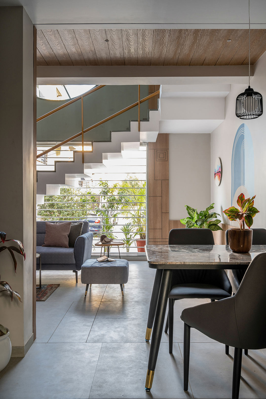 Modern, open-concept living space with marble dining table, plush seating, and lush greenery.