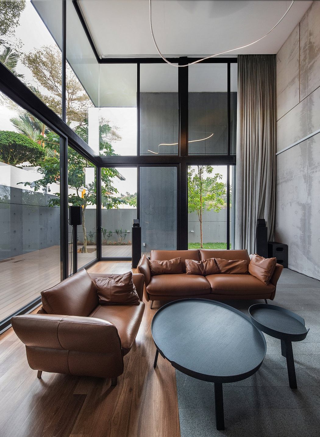Modern living room with floor-to-ceiling glass walls, leather sofas, and round coffee tables.