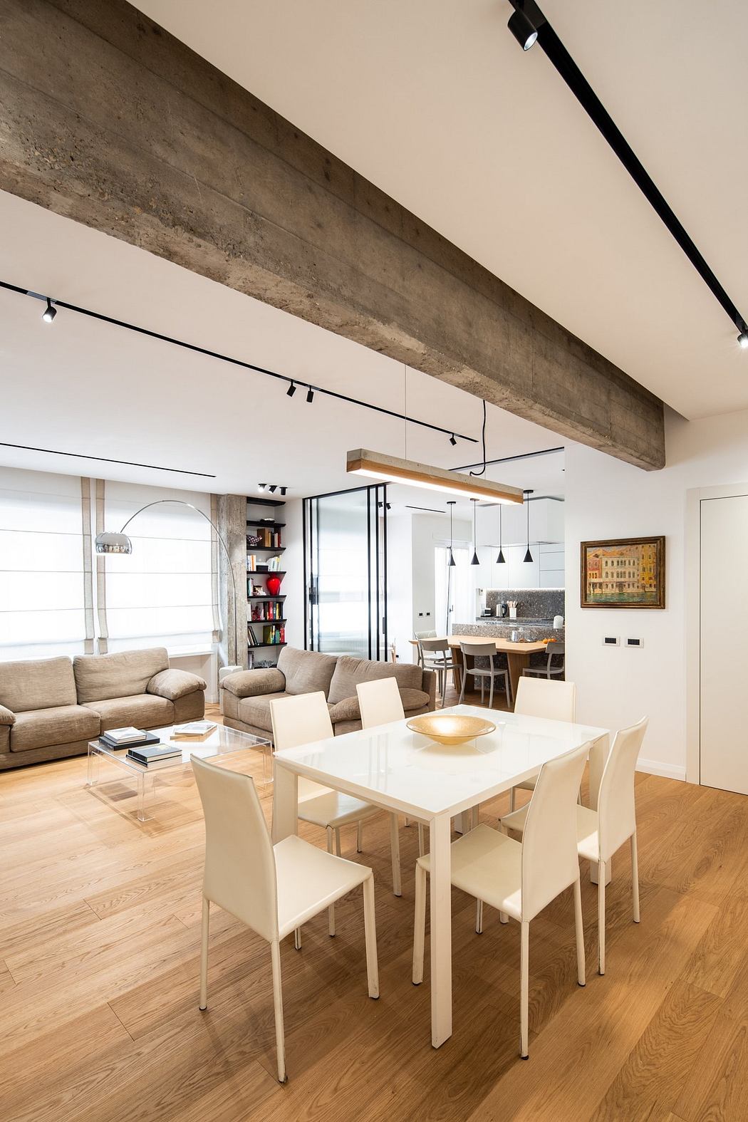 The image showcases a modern open-plan living space with a concrete ceiling beam, track lighting, and sleek furniture.