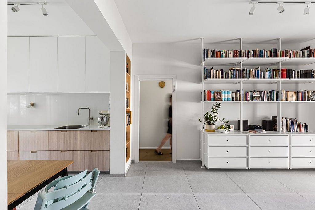 Modern open-plan kitchen and living area with built-in bookshelves, light wood and white tones.